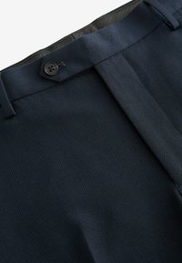 Pantalones de color azul marino oscuro hechos de una tela texturizada. Presentan una parte frontal plana, un cierre de botón y un sutil patrón tejido.