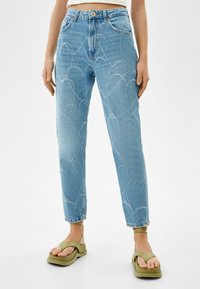 Ljusblå denimjeans med ett hjärtformat sömmönster, hög midja och rak passform. Kombinerad med olivgröna sandaler.