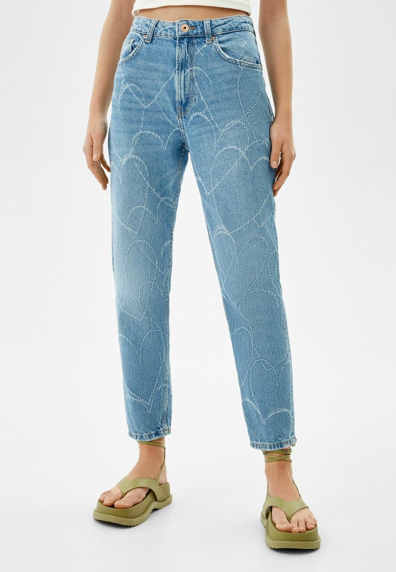 Ljusblå denimjeans med ett hjärtformat sömmönster, hög midja och rak passform. Kombinerad med olivgröna sandaler.
