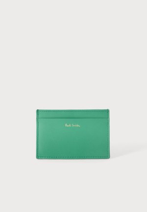 Zelený kožený držiak na karty s dvoma priehradkami na karty a zlatým logom „Paul Smith“ v strede prednej strany na jednoduchom svetlom pozadí.
