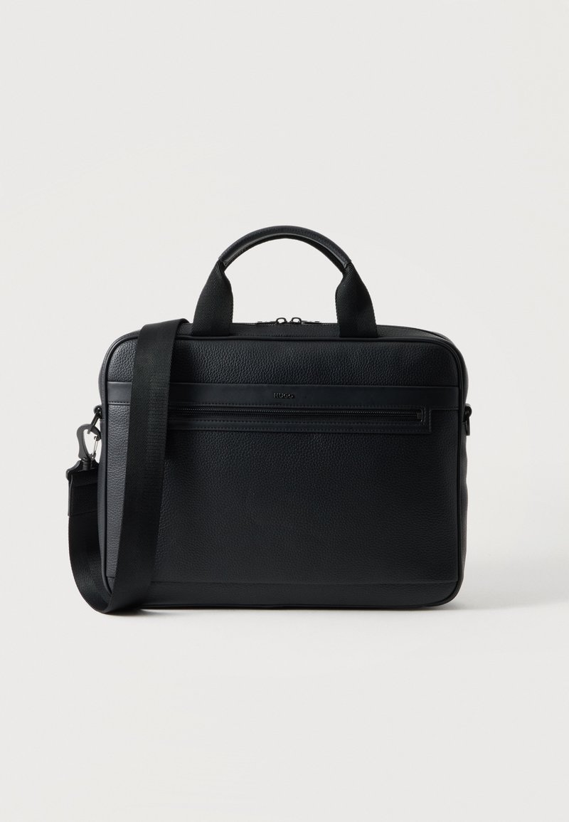 Porte-documents noir en cuir grainé, avec des poignées sur le dessus, une bandoulière amovible et une poche zippée à l’avant, sur fond clair.