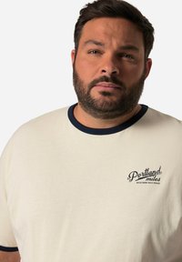 Cremefarvet bomulds T-shirt med marineblå krave og logo på venstre bryst, der lyder "Portland miles Western Railroad." Blød tekstur, afslappet pasform.