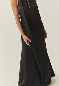 Vestido largo de satén negro con una abertura alta y escote en forma de ojo de cerradura, con una silueta fluida y una textura suave.