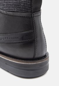 Černá kožená bota s texturovaným textilním svrškem, kontrastním prošíváním a gumovou podrážkou. Obsahuje logo vyražené na boční straně.