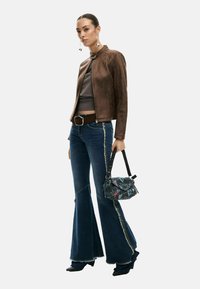 Pruun seemisnahast pommitaja jope, hall silutud top, lõhikutega helerohelised teksad ja must mustriga käekott rihmaga.