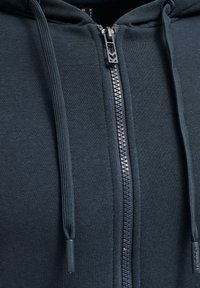 Mörkblå zip-up hoodie i mjukt tyg med en texturerad yta, som har en silverfärgad dragkedja och matchande snoddar.