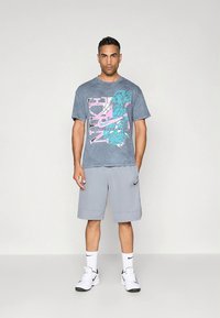 Grå T-shirt med farverigt "Nike" grafik og shorts, begge lavet af letvægtsstof; sneakers med sorte detaljer og hvide sokker.