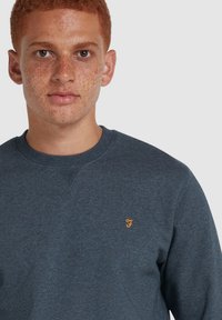 Donkerblauwe sweatshirt met een ronde hals en geribde manchetten. Bevat een klein oranje logo op de borst. Zacht, gestructureerd materiaal.