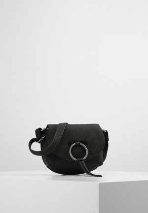 Zwarte crossbodytas met een textuur, klepsluiting en een decoratieve zilveren ring aan de voorkant, rustend op een wit voetstuk tegen een effen achtergrond.