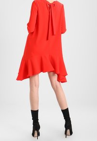 Vestido rojo hasta la rodilla con mangas largas, bajo con volantes y un lazo en la parte posterior. Llevado con calcetas negras hasta la rodilla y tacones.