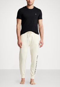 Svart bomullst-skjorte med rund hals og liten logo; kremfargede joggebukser med elastisk liv og sidetrykk av logo i svart.