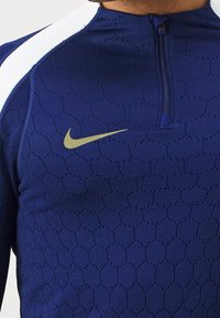 Navy zip-up athletic top with a textured hexagonal pattern, features white accent stripes and a gold Nike logo on the chest.