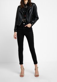 Svart läderbikerjacka med silverdragkedja, blommig blus under, högmidjade svarta skinny jeans och nakna klacksandaler.