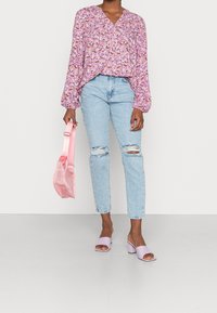 Blouse à manches longues à fleurs rose et violet, jean déchiré bleu clair, sac rose pastel et mules à talon bloc lavande.