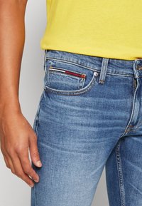 Jeans di denim azzurro chiaro con un classico design a cinque tasche. Rivetti e cuciture visibili; t-shirt gialla parzialmente visibile sopra.