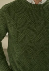 Pull en tricot vert avec un motif chevron texturé, des poignets côtelés et un col rond. Matériau doux au toucher chaleureux.