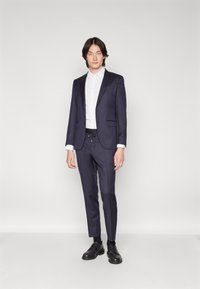Navy suit with a tailored blazer and slim-fit trousers. White button-up shirt and black leather shoes complete the look.