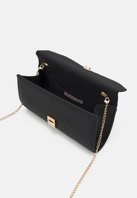 Sac à main en similicuir noir avec un rabat ouvert, une bandoulière en chaîne dorée et une fermeture carrée magnétique. Poche intérieure visible.