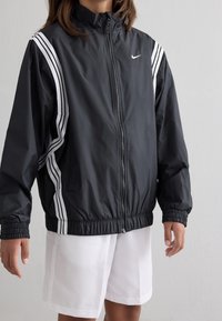 Black nylon windbreaker jacket with white striped accents along the shoulders and a zip closure, featuring an elastic hem and cuff.