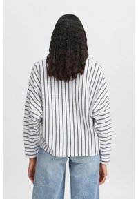 Donna di spalle che indossa un maglione bianco a maniche lunghe con righe verticali blu navy e jeans a gamba larga di un blu chiaro.