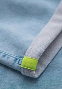 Tela azul clara con un puño texturizado gris acentuado por una banda verde brillante. Detalles de costura visibles a lo largo del borde.
