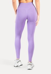  Paar paarse leggings gemaakt van rekbaar materiaal, met een hoge tailleband en een naadloos ontwerp. Gecombineerd met witte atletische sneakers.