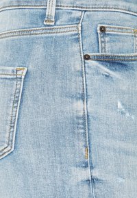 Jeans de mezclilla azul claro con una textura desgastada. Incluye bolsillos traseros estándar con costuras en contraste y remaches de metal.