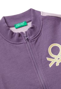 Sudadera morada con cremallera y cuello acanalado, etiqueta verde de "United Colors of Benetton" y un logo dorado con purpurina en el pecho.