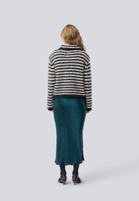 Maglione a righe in nero e crema, abbinato a una gonna a sottoveste in satin teal. Caratterizzato da una vestibilità rilassata e una lunghezza cropped. Tacchi neri con fibbie.