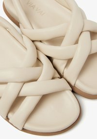 Beige sandalen met een kruislingse ontwerp van soepel leer. Platte zool met een lichtbruine rubberen basis en subtiele branding.
