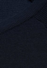 Donkerblauwe gebreide stof met een gestructureerd patroon. De close-up toont ribbelachtige randen en subtiele variaties in de draaddikte.