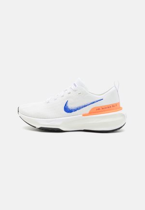 Weißer Sportschuh mit atmungsaktivem Strick-Obermaterial, blauer Swoosh, schwarzer Außensohle und orangefarbenem Akzent in der Zwischensohle. Verfügt über gestickte Details und Schnürverschluss.