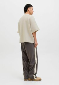 Beige overméretezett póló rövid ujjakkal, szürke, szűkülő nadrággal, amely krém színű oldalsávokkal rendelkezik, és bézs slip-on cipővel párosítva.