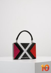 Borsa rettangolare scintillante con motivi geometrici rosa, rossi, neri e bianchi; manico nero; accenti metallici; marchio visibile.