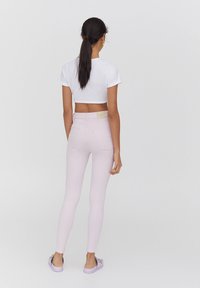 Jean rose clair à coupe ajustée, avec des poches arrière et une petite étiquette de marque à la taille. Associé à un t-shirt blanc court.