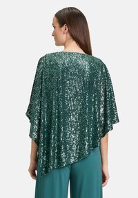 Poncho verde con paillettes, dal design morbido e drappeggiato, con orlo alto-basso. Presenta paillettes luccicanti e strutturate su tutta la superficie.