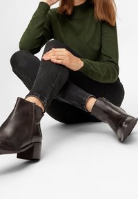 Zwarte leren enkellaarzen met een chunky hak, met een gladde textuur en een minimalistisch ontwerp. De outfit bestaat uit een groene top en donkere jeans.