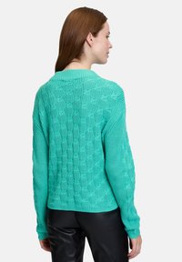 Türkisfarbener Strickpullover mit strukturiertem Wabenmuster, geripptem Kragen und überschnittenen Schultern, kombiniert mit schwarzen Lederhosen.
