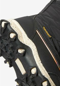 Schwarzer Wanderschuh mit einem gesteppten Obermaterial, Gummisohle mit multidirektionalen Stollen und einer beigen gesprenkelten Zwischensohle. HydroGuard-Logo sichtbar.
