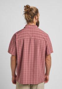 Camicia a maniche corte con bottoni di colore rosso chiaro e motivo a griglia. Presenta un colletto e una cucitura a yoke sul retro, realizzata in tessuto leggero.