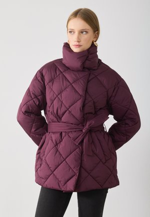 Quiltad pufferjacka i djup burgund med hög krage, bältad midja och diagonalt stygnmönster. Slät textur, medellång design.