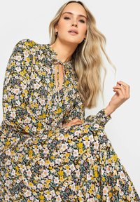 Vestido floral con un patrón en amarillo, rosa y blanco sobre un fondo negro. Manga larga y escote fruncido con un detalle de lazo.