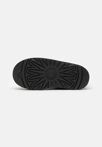 Suela de zapato negra con un diseño texturizado y estampado que presenta un motivo central de explosión de estrellas y bordes acanalados para mayor tracción.