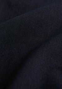 Tmavě modrá látka s hladkou texturou, s mírným leskem a minimální pružností, zachycená ve vlnitém, složeném tvaru.