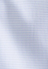 Tessuto di un blu chiaro con una texture e un motivo geometrico, caratterizzato da piccole forme interconnesse. La superficie sembra liscia e tessuta.