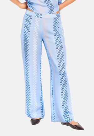 Lyseblå vide bukser med vertikale striper og kjedemønstre i marineblått, hvitt og fersken, brukt med svarte spisse sko.