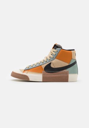 High-top sneaker met beige veters, oranje en turkooizen panelen, zwarte Nike-swoosh en een getextureerde bruine en witte zool tegen een witte achtergrond.
