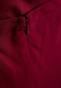 Bordeaux-kangas, jossa on teksturoitu pinta, ja huomaamaton vetoketju sivulla, korostaen puhtaita linjoja ja minimalistista muotoilua.