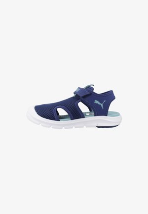 Sandalia infantil Puma azul marino con parte superior de malla, tira ajustable con velcro, logo azul claro, plantilla acolchada color azul verdoso y suela blanca flexible.