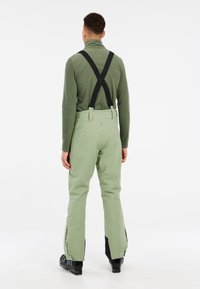Pantalons de ski verts avec bretelles noires ajustables, design à jambe droite et ouvertures à la cheville zippées. Texture douce, matériau résistant à l'eau.